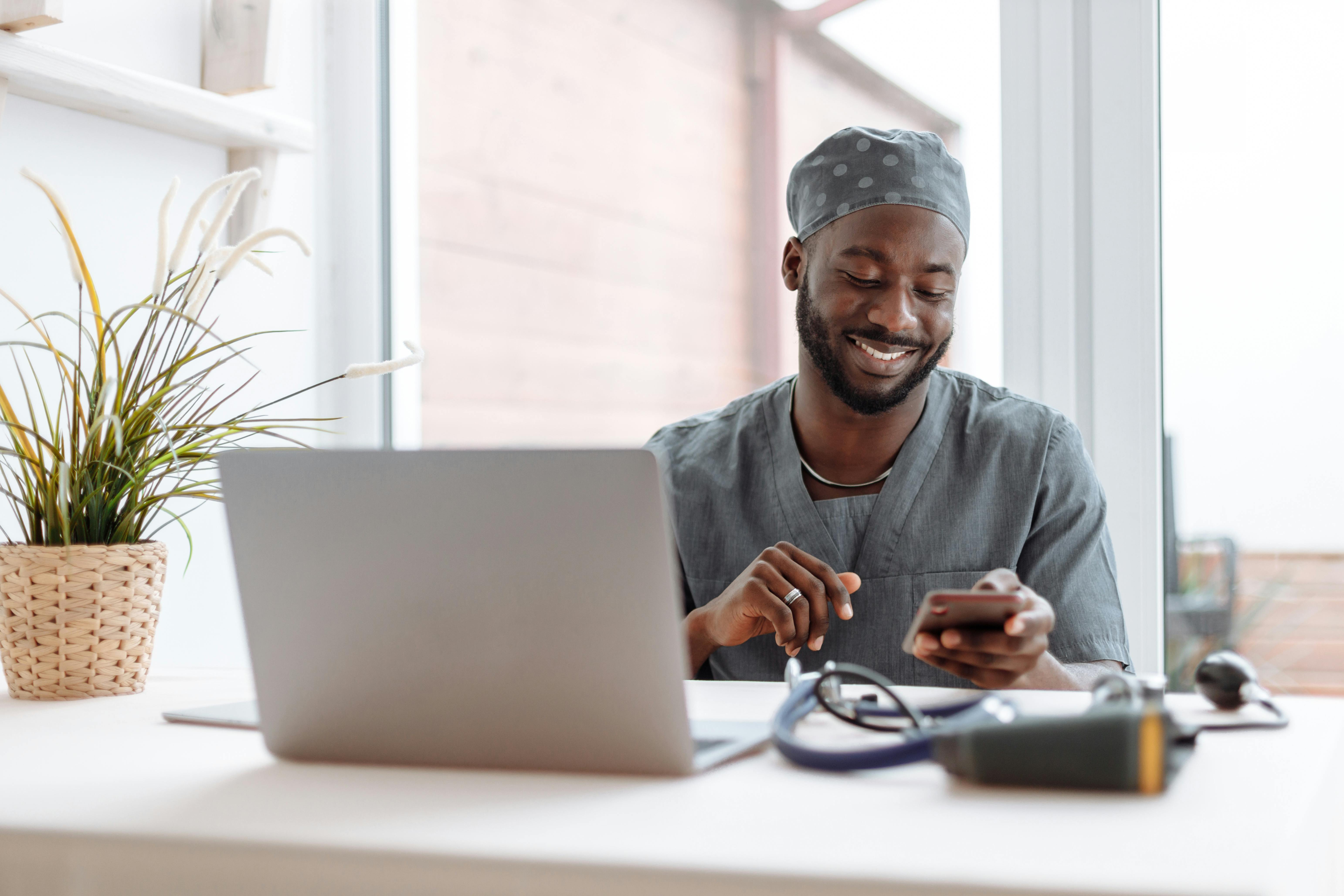 Professionnel de santé souriant utilisant un smartphone et un ordinateur portable